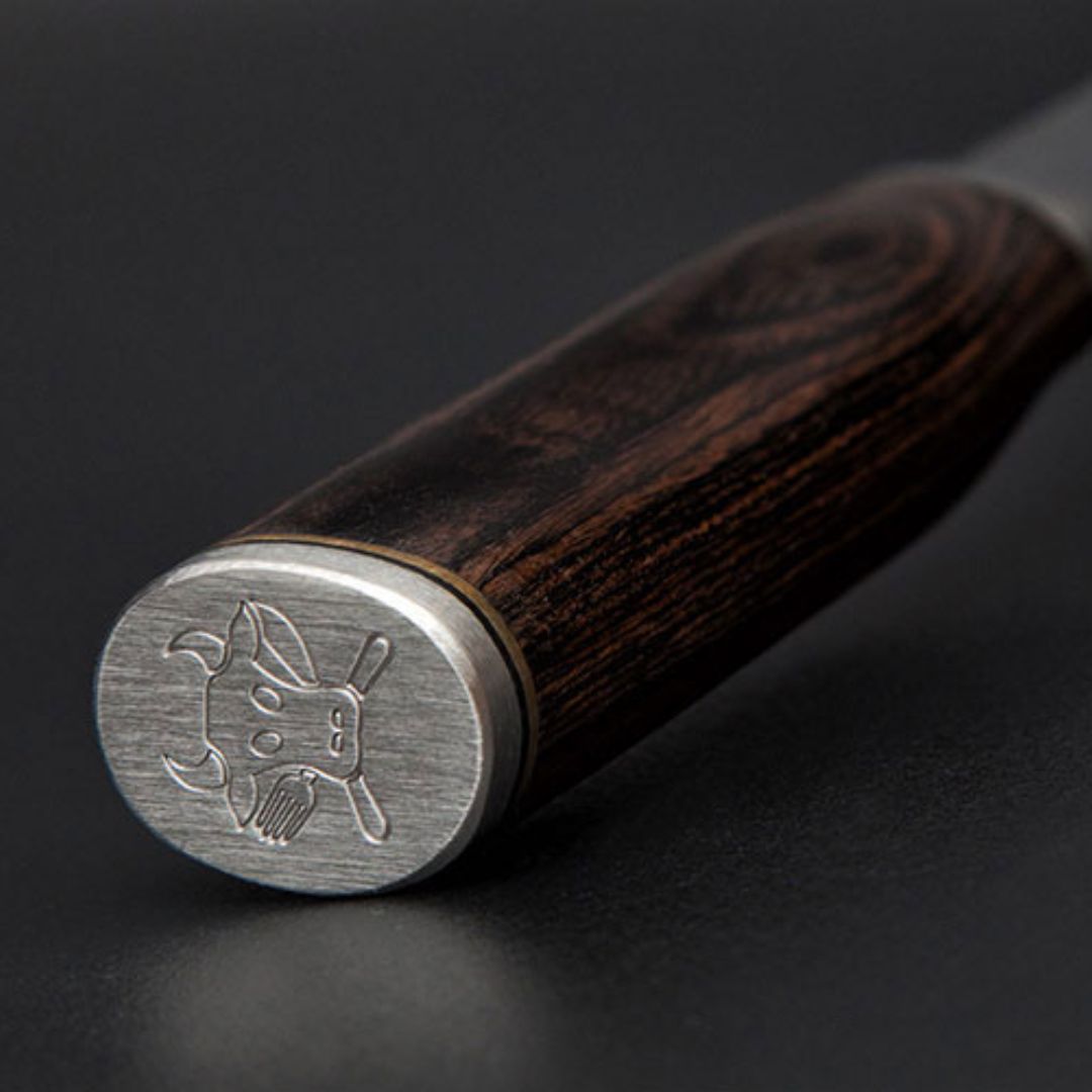 Nahaufnahme des Griffs des Kai Shun Tim Mälzer Santoku TDM-1702, mit dunklem Holzfinish und einer Endkappe aus Metall, auf der ein Stierkopf und gekreuzte Baseballschläger eingraviert sind. Klinge 18 cm, Edition "THE MAGIC KAI WISHLIST".