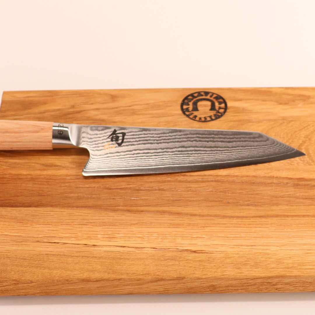 Auf dem mitgelieferten Eichenholzbrett ruht ein Kai Shun Classic White Kiritsuke - Limitierte Edition (5.555 St.), das sich durch hochwertige Handwerkskunst und elegantes Design auszeichnet.