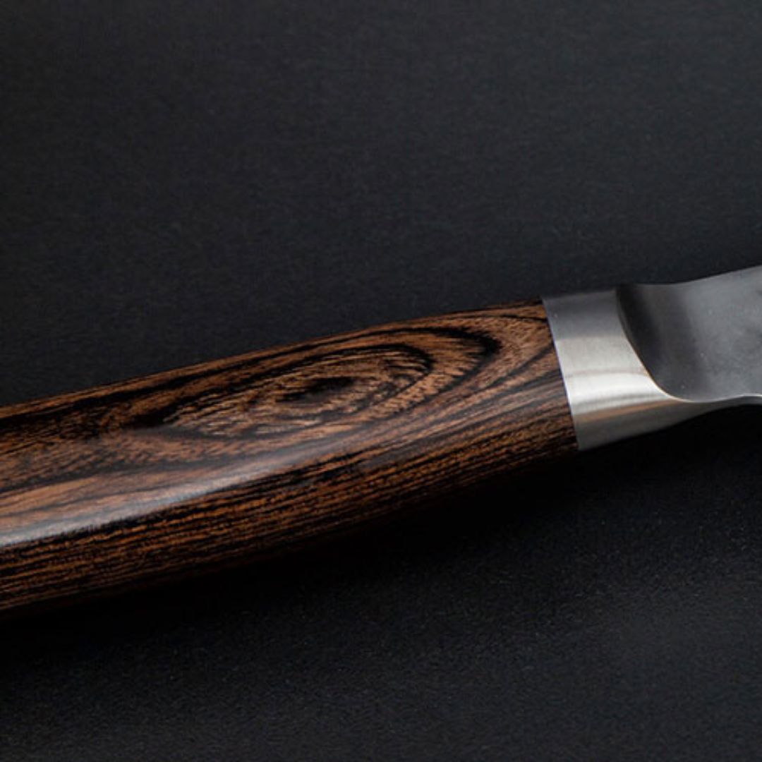 Eine Nahaufnahme des Kai Shun Tim Mälzer Santoku TDM-1702 (18 cm Klinge, "THE MAGIC KAI WISHLIST") mit dunklem Holzgriff und Metallhals vor schwarzem Hintergrund.