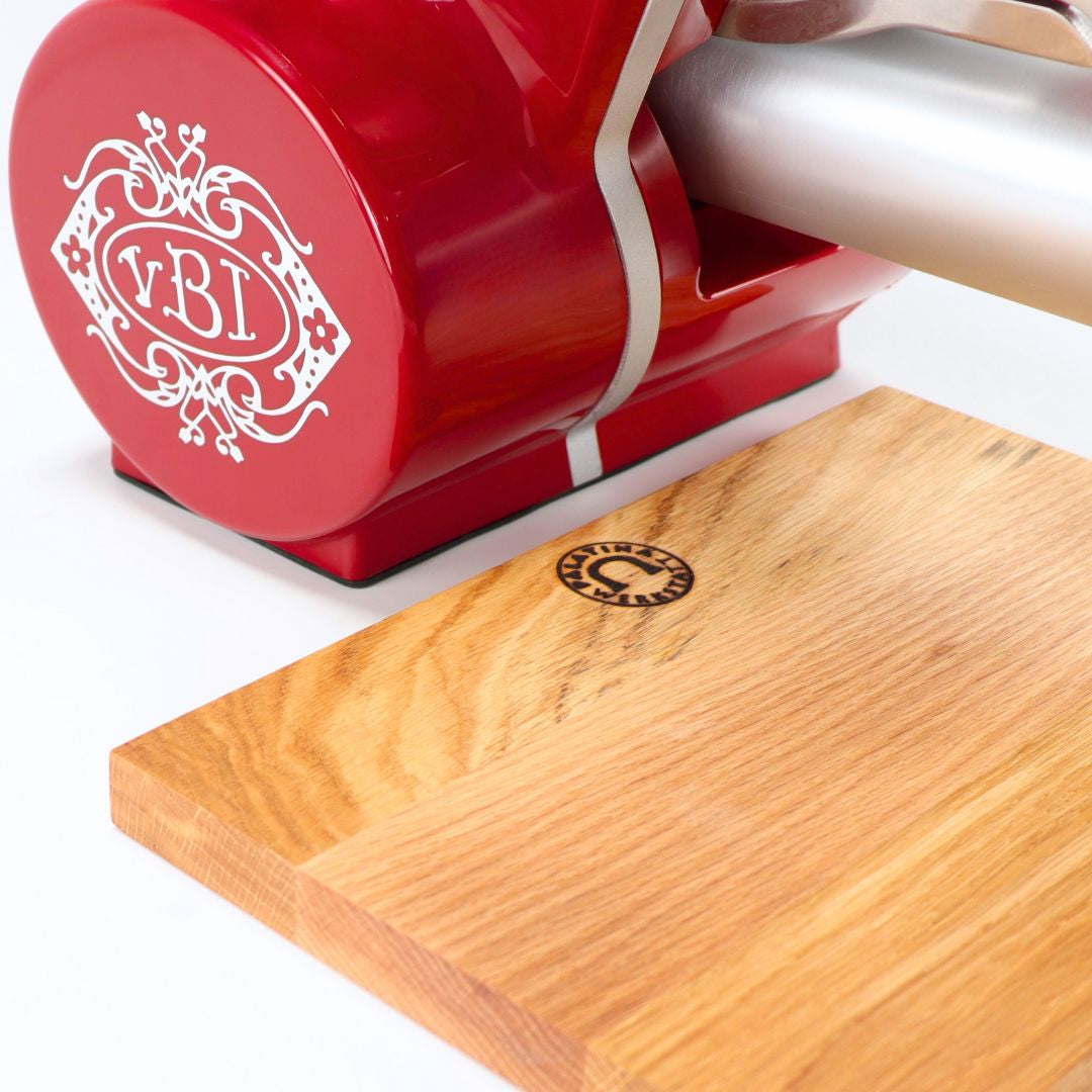 Eine Nahaufnahme des roten Berkel Icon Line 170 mit weißem Logo neben einem handgefertigten 30x20 cm großen Eichenholzschneidebrett, beide auf weißem Hintergrund.