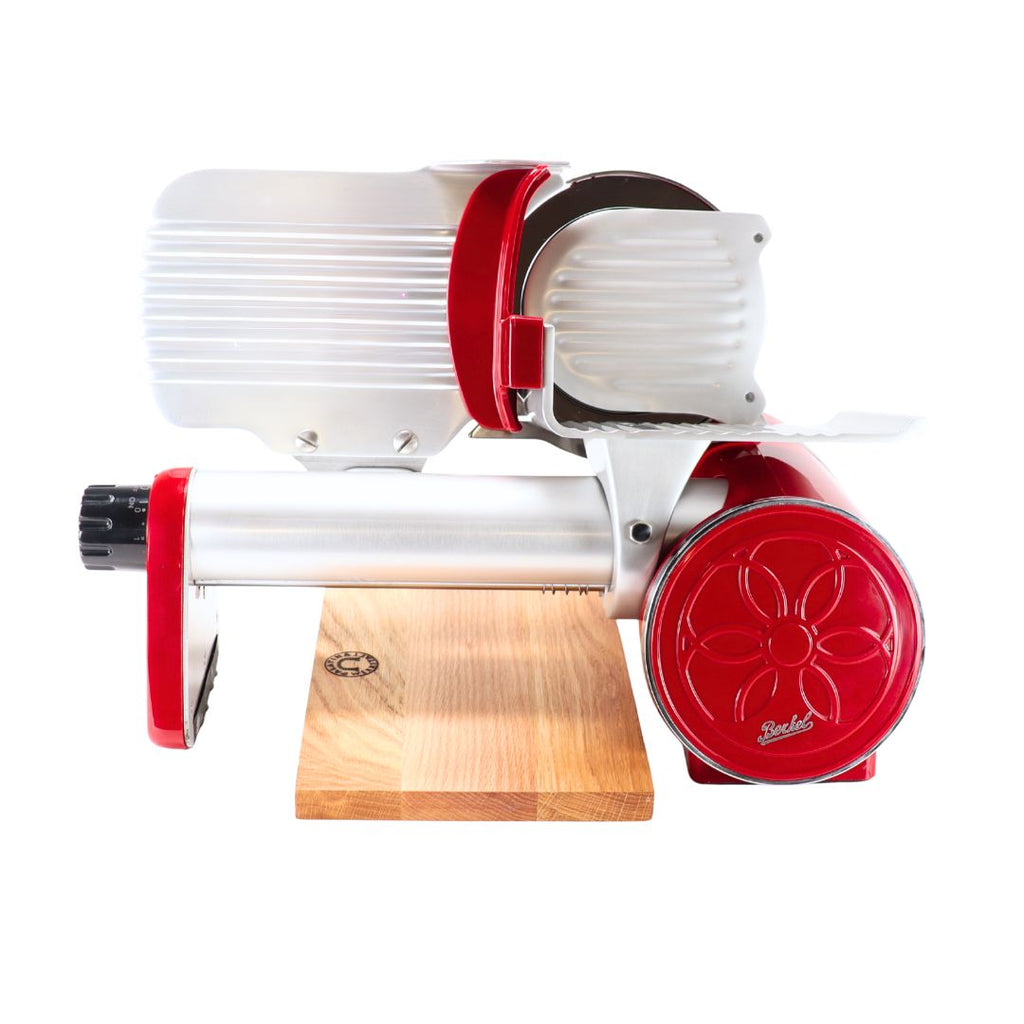 Eine Berkel Icon Line 170 in rot mit handgefertigtem Eichenholz-Einlegebrett (30x20cm) steht seitlich auf dem Brett, zeigt Klingenrad, Griff und Retro-Design.