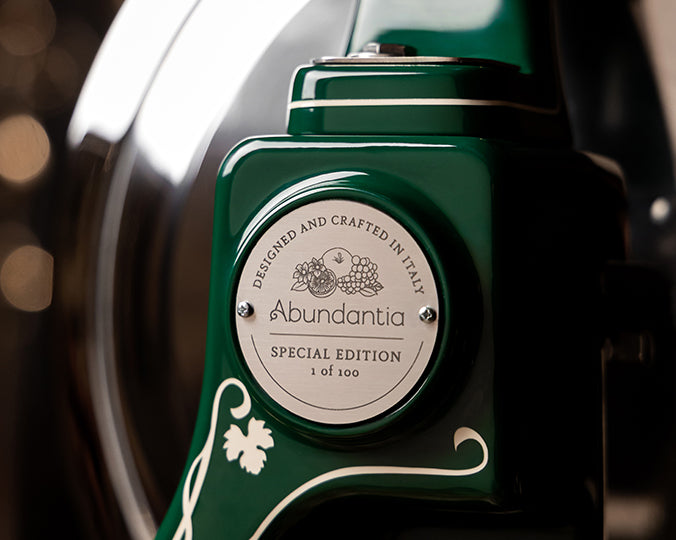 Nahaufnahme einer grünen Berkel Volano B114 Sondermodell Schwungradmaschine incl. Standfuß + Fassholzbrett mit einer Metallplakette "Abundantia Special Edition 1 of 100. Designed and crafted in Italy", mit Weintrauben und Weinreben-Akzenten.