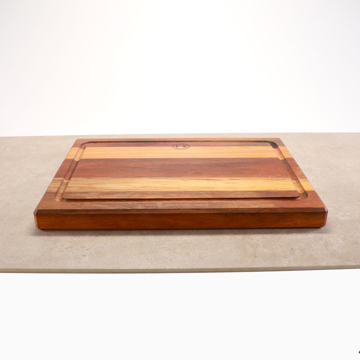 Ein Palatina Küchenbrett mit Saftrille 40x30 cm aus Weinfassholz, das verschiedene Brauntöne aufweist, liegt auf einer hellen Oberfläche. Das Schneidebrett hat an den Rändern eine geschnitzte Saftrille, um Saft aufzufangen. Der schlichte weiße Hintergrund hebt die Holzmaserung und -struktur des Bretts wunderschön hervor.