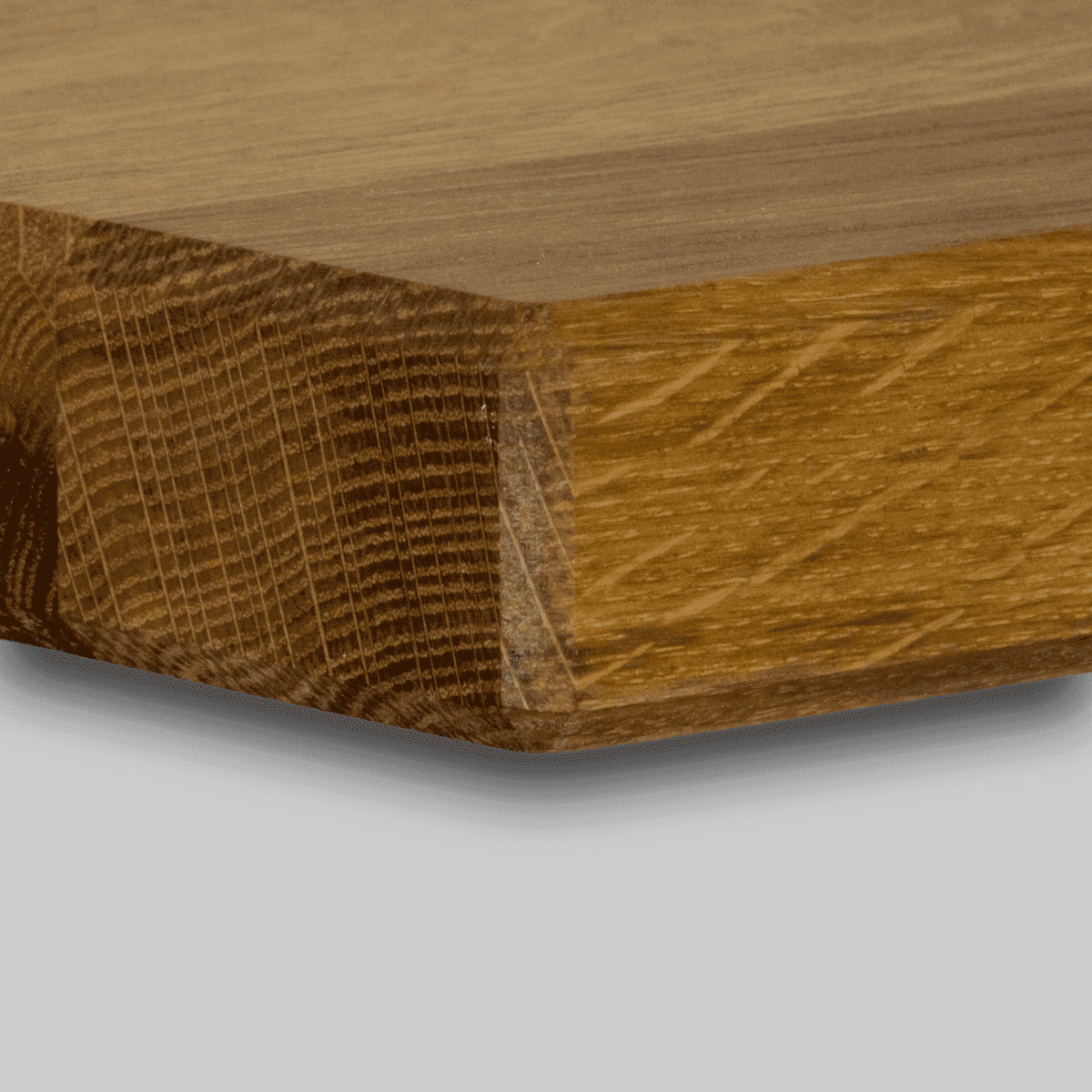 Nahaufnahme der Ecke eines Holzstücks mit abgeschrägter Kante, die Maserung und Struktur zeigt. Das Küchen-Schneidebrett 40 x 30 cm aus Holz von alten Weinfässern hat eine glatte, polierte Oberfläche und steht vor einem schlichten, hellgrauen Hintergrund.