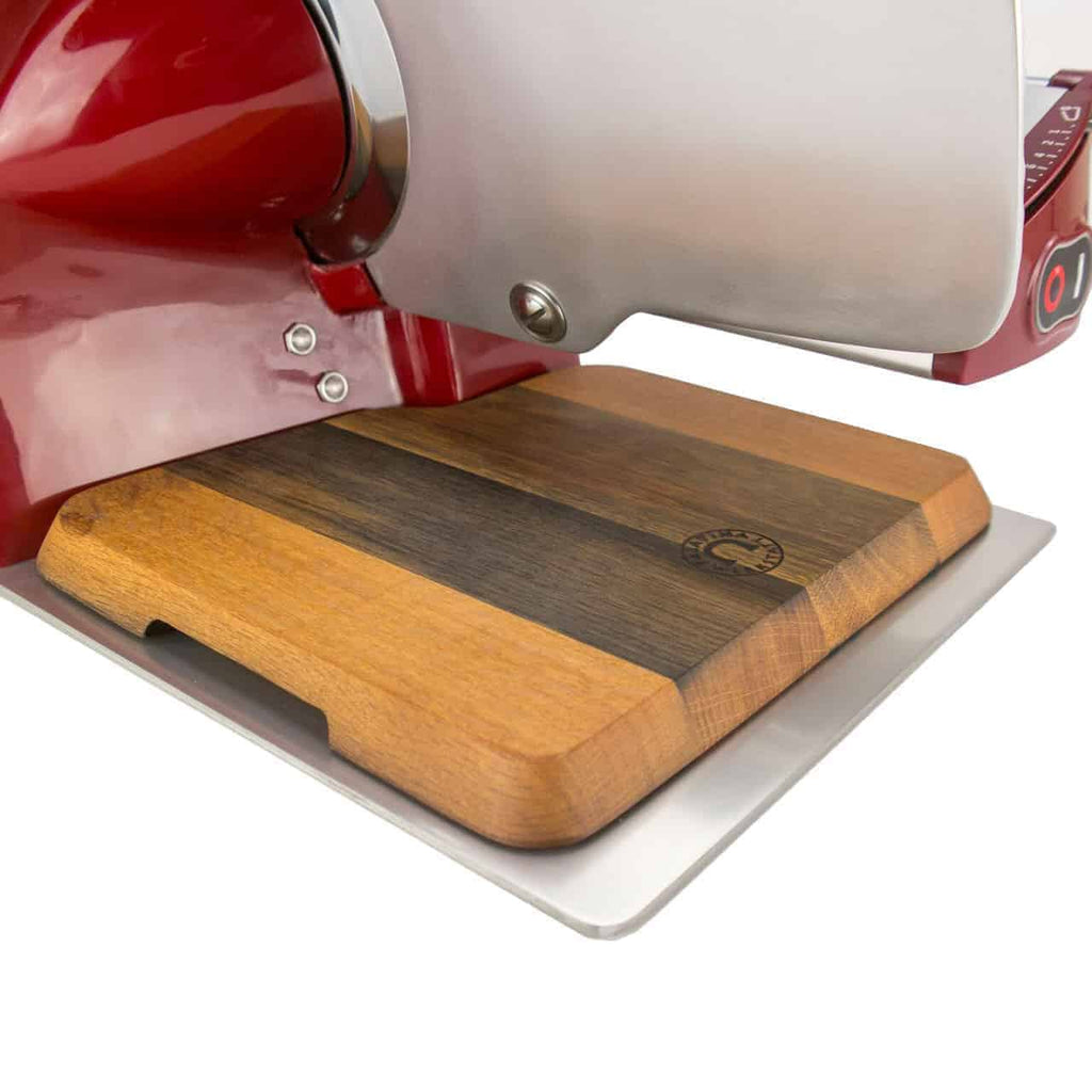 Eine Nahaufnahme einer roten elektrischen Aufschnittmaschine Berkel Home Line 200 mit einem handgefertigten Fassholz-Einlegebrett von Palatina Werkstatt. Das Schneidebrett hat ein zweifarbiges Holzfinish mit einem geätzten Logo in der Ecke und die Schneideklinge ist teilweise sichtbar. Der Aufbau erfolgt auf einer weißen Oberfläche.