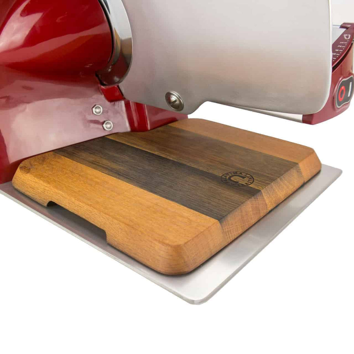 Eine Nahaufnahme einer roten elektrischen Aufschnittmaschine Berkel Home Line 200 mit einem handgefertigten Fassholz-Einlegebrett von Palatina Werkstatt. Das Schneidebrett hat ein zweifarbiges Holzfinish mit einem geätzten Logo in der Ecke und die Schneideklinge ist teilweise sichtbar. Der Aufbau erfolgt auf einer weißen Oberfläche.