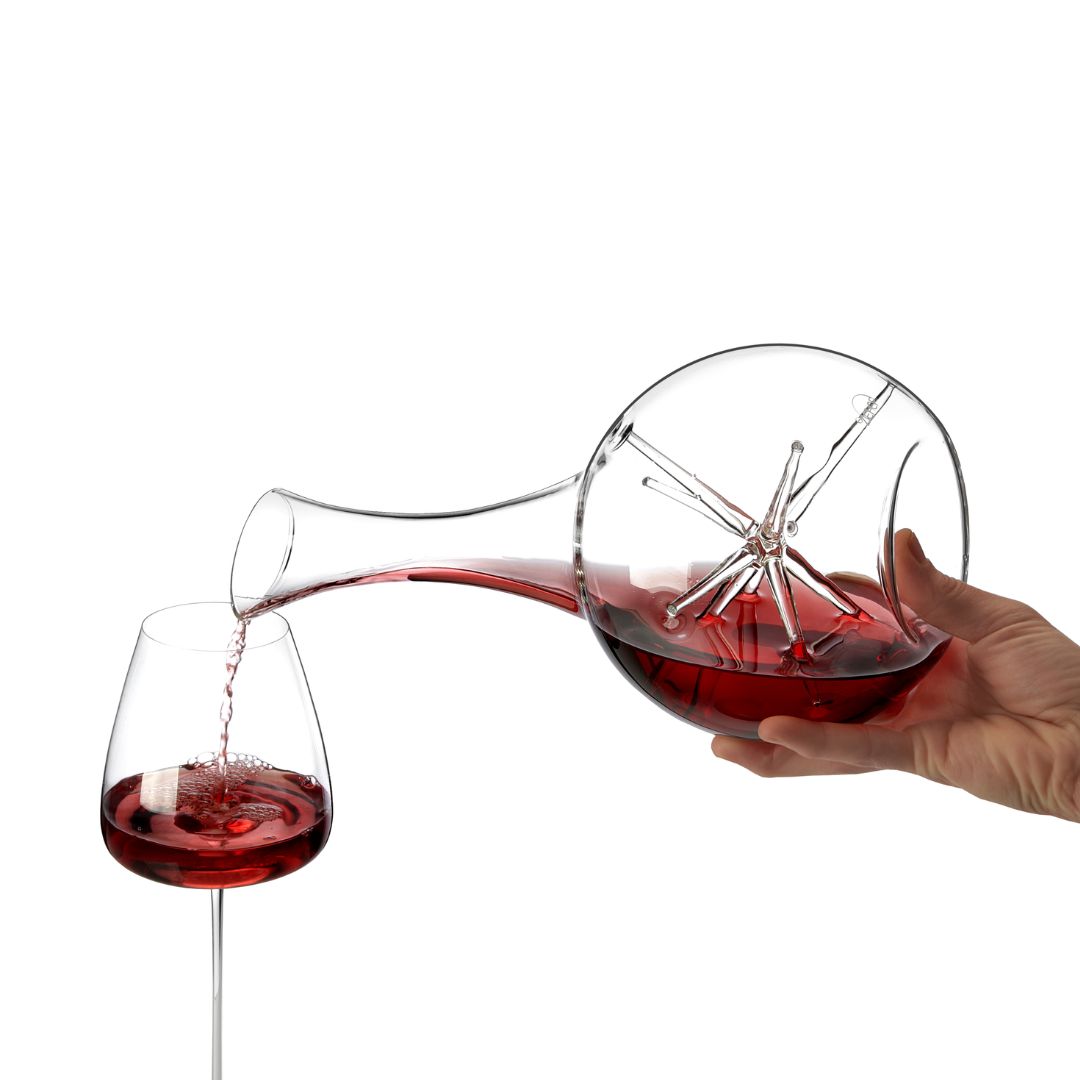Eine Hand schenkt Rotwein aus dem Weindekanter "Star" - Exklusive Karaffe mit Sternendesign | 34 cm- Zieher ein. Das elegante Sternmuster hebt sich von einem schlichten weißen Hintergrund ab, während der Wein das Glas füllt.