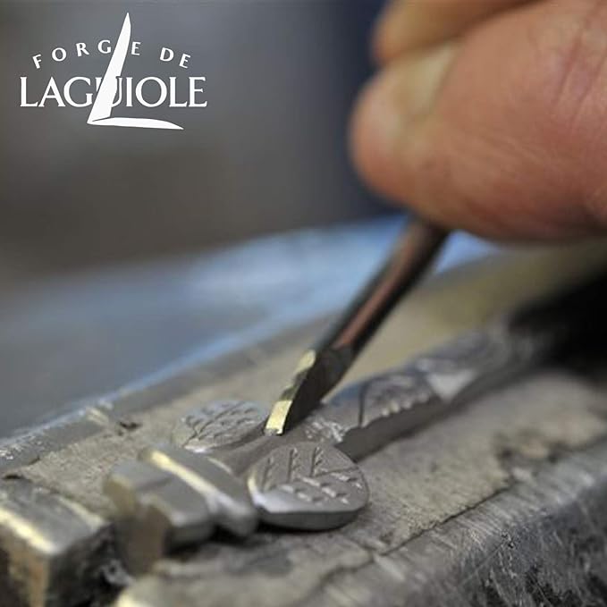Ein Handwerker graviert mit einem kleinen Werkzeug auf einer Werkbank sorgfältig komplizierte Muster in Metall und fertigt so gekonnt etwas, das wie ein Teil eines dekorativen Forge De Laguiole Kellnermesser Sommelier | Wacholder matt aussieht. Das Logo „Forge de Laguiole“ ist prominent in der oberen linken Ecke angebracht und symbolisiert außergewöhnliche Qualität und Kunstfertigkeit.