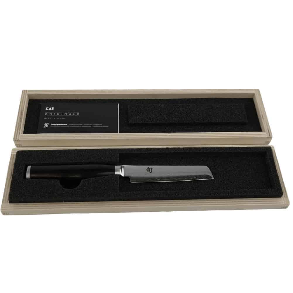 Ein elegantes Kai Shun Premier Minamo TMM-0700 Kochmesser mit dunklem Griff wird in einer offenen Holzbox präsentiert, die mit schwarzem Schaumstoff ausgekleidet ist. Im Deckel der Box befindet sich ein Etikett. Die Gesamtpräsentation unterstreicht die Qualität und Handwerkskunst des Messers, ergänzt durch eine 9 cm lange Klinge aus Damaszenerstahl und ein Küchenbrett aus Eichenholz mit den Maßen 30 x 22 cm.