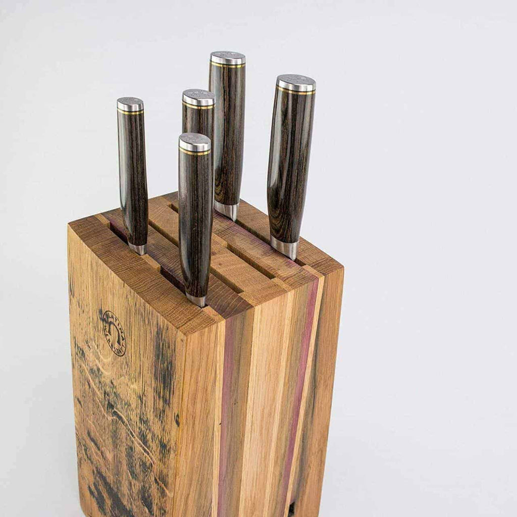 Ein Messerblock aus altem Weinfass, bestückt mit fünf hochwertigen KAI Shun Tim Mälzer Damastmessern, die sauber eingelegt sind. Der Block hat ein natürliches Holzfinish, das an ein rustikales Weinfass erinnert, und die Messergriffe sind dunkel mit metallischen Enden. Das Bild zeigt einen schlichten, hellen Hintergrund.