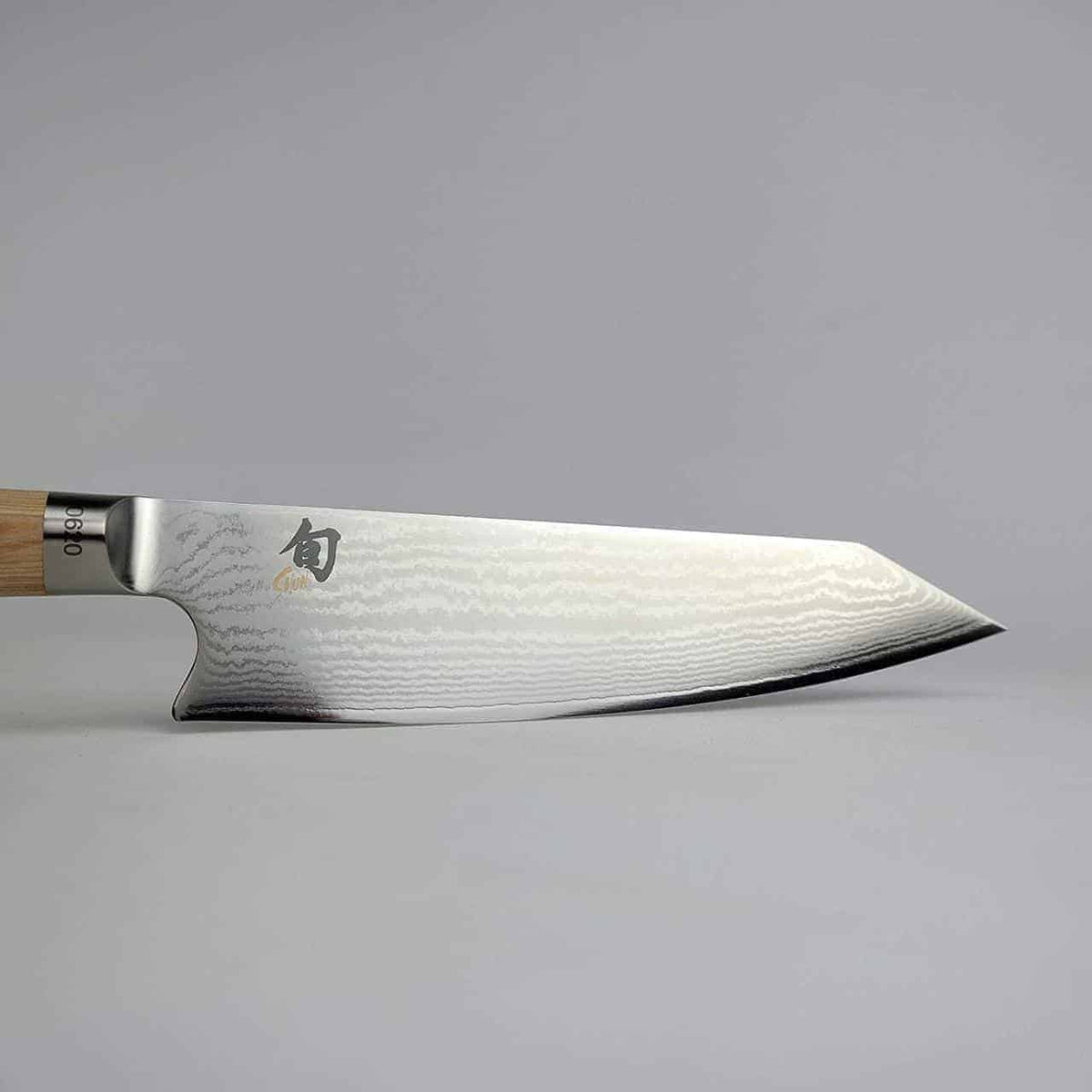 Ein schlankes, scharfes Kiritsuke-Messer Kai Shun Classic White DM 0777W in limitierter Auflage mit Holzgriff und polierter Klinge mit wellenförmigem Muster. Der Hintergrund ist schlicht und hellgrau und betont die Form und das Design des Messers. Komplett mit einem handgefertigten Holzschneidebrett von 30 x 18 cm verkörpert dieses Set Eleganz sowohl in der Handwerkskunst als auch in der Ästhetik.