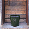 Der glasierte Pflanzkübel „Garden Green“ (Höhe 19–38 cm) glänzt auf einer Steinstufe vor einer rustikalen Holztür mit Metallelementen.