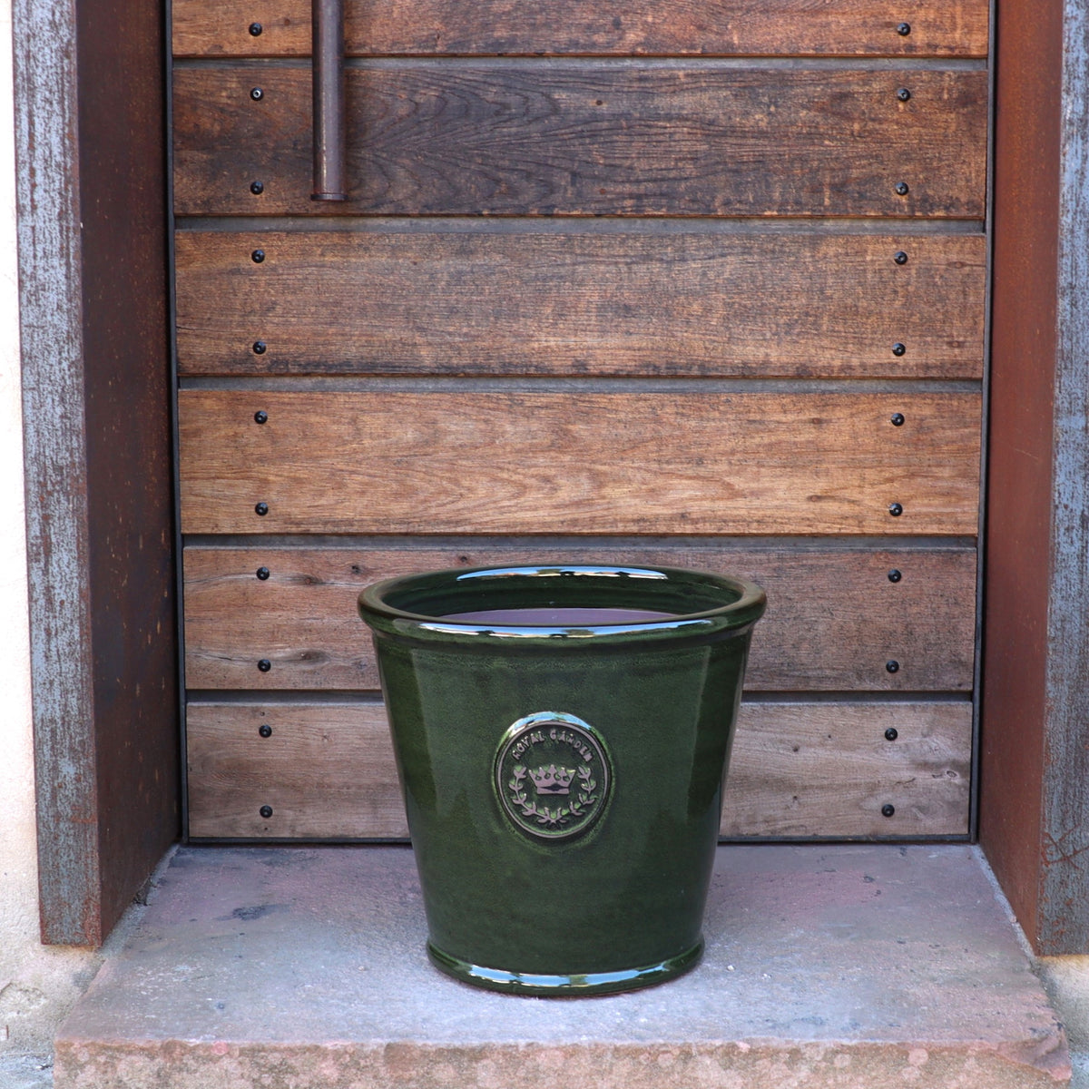 Der glasierte Pflanzkübel „Garden Green“ (Höhe 19–38 cm) glänzt auf einer Steinstufe vor einer rustikalen Holztür mit Metallelementen.