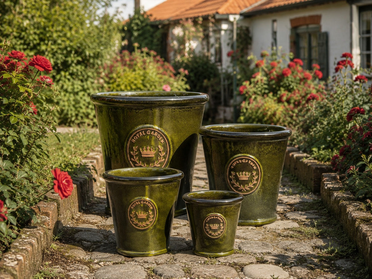 Vier glasierte Pflanzkübel in der Farbe „Garden Green“ (Höhe 19–38 cm) sind in verschiedenen Größen auf einem Gartenweg aus Stein ausgestellt, umgeben von roten Rosen und Grünpflanzen, im Hintergrund ist ein Haus zu sehen.