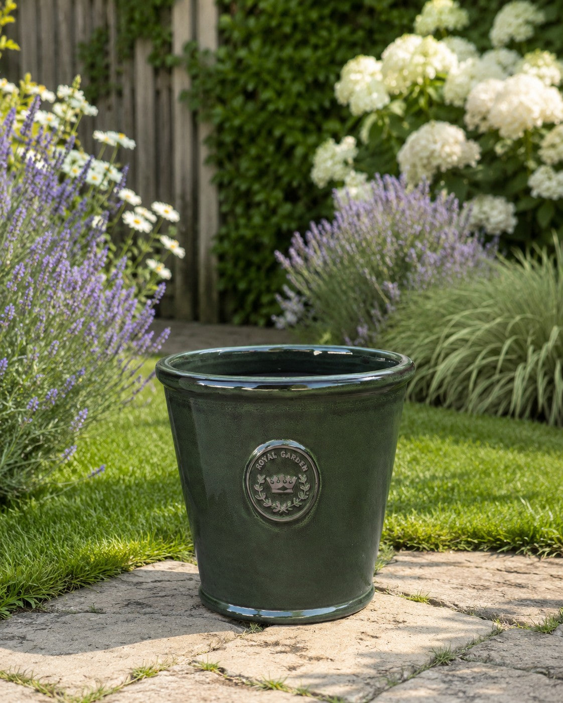 Der glasierte Pflanzkübel „Garden Green“ (Höhe 19 bis 38 cm) steht auf einer Steinterrasse im Garten, umgeben von Lavendel, weißen Hortensien und Ziergras vor einem Holzzaun.