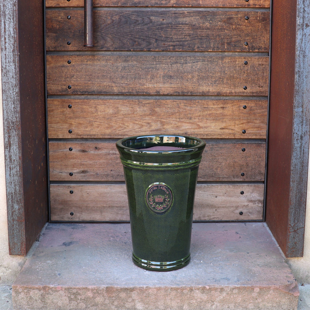 Die Vasenform "Royal Garden Green" (Höhe 33-51 cm), eine hohe grüne Keramikvase, steht auf einer steinernen Türschwelle vor einer Holztür mit Paneelen und Metallakzenten und erinnert an den zeitlosen Charme der Azur-Provence.