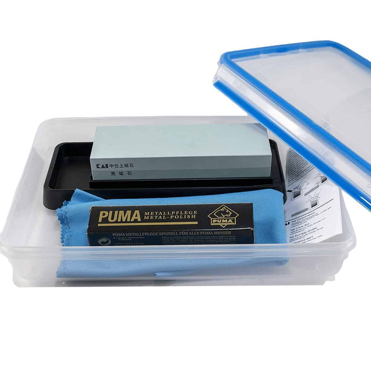 Ein Schleifset, Kai 4-teiliges Schleif- und Pflegeset, mit einem AP-0305 Schleifstein-Kombinationsschleifstein in einer Plastikbox mit durchsichtigem Deckel. Das Set enthält einen grünen Kombinationsschleifstein auf einer schwarzen Basis, ein blaues Reinigungstuch mit der Aufschrift „PUMA“ und eine gefaltete Gebrauchsanweisung. Der Behälter hat einen Deckel mit blauem Rand, der teilweise geöffnet ist.