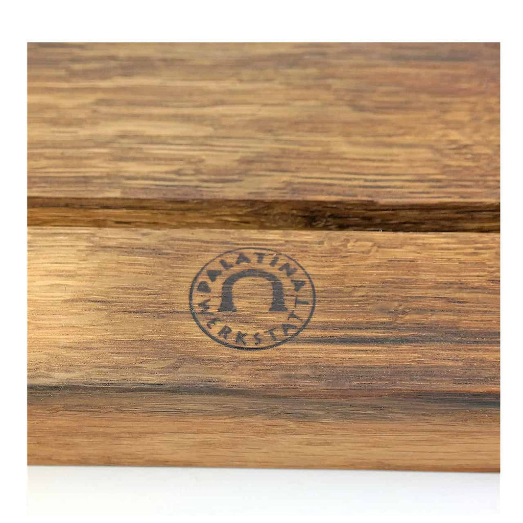 Nahaufnahme einer Holzoberfläche mit einem eingeprägten dunklen Logo. Das Logo hat eine auffällige Hufeisenform, umgeben von den Worten „Palatina Werkstatt“. Das Holz weist eine natürliche, rustikale Textur mit sichtbaren Maserungen auf und fängt den Charme dieses handgefertigten Tablethalters von Palatina Werkstatt perfekt ein.