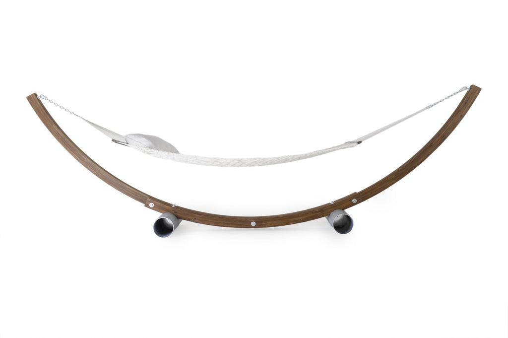 Eine minimalistische Hängematte mit Unterteil aus galvanisiertem Stahl mit einem Bett aus weißem Stoff hängt anmutig an einem geschwungenen Holzrahmen. Der Ständer, der für zusätzliche Stabilität von robusten zylindrischen Beinen aus galvanisiertem Stahl getragen wird, ruht auf einem schlichten weißen Hintergrund.