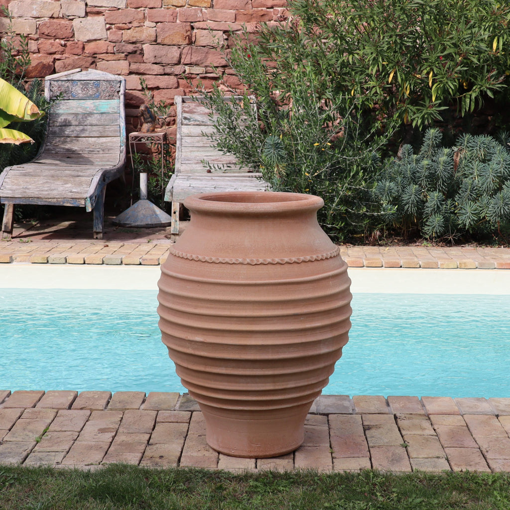Die frostfeste Amphore "Agave", H=80cm, Terrakotta-Topf, steht auf einer Steinterrasse an einem hellen Pool, flankiert von zwei hölzernen Liegestühlen und üppigem Grün im Hintergrund.