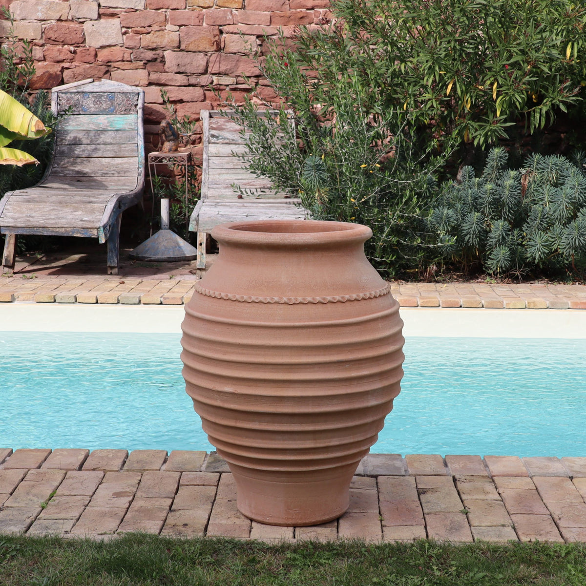 Die frostfeste Amphore "Agave", H=80cm, Terrakotta-Topf, steht auf einer Steinterrasse an einem hellen Pool, flankiert von zwei hölzernen Liegestühlen und üppigem Grün im Hintergrund.