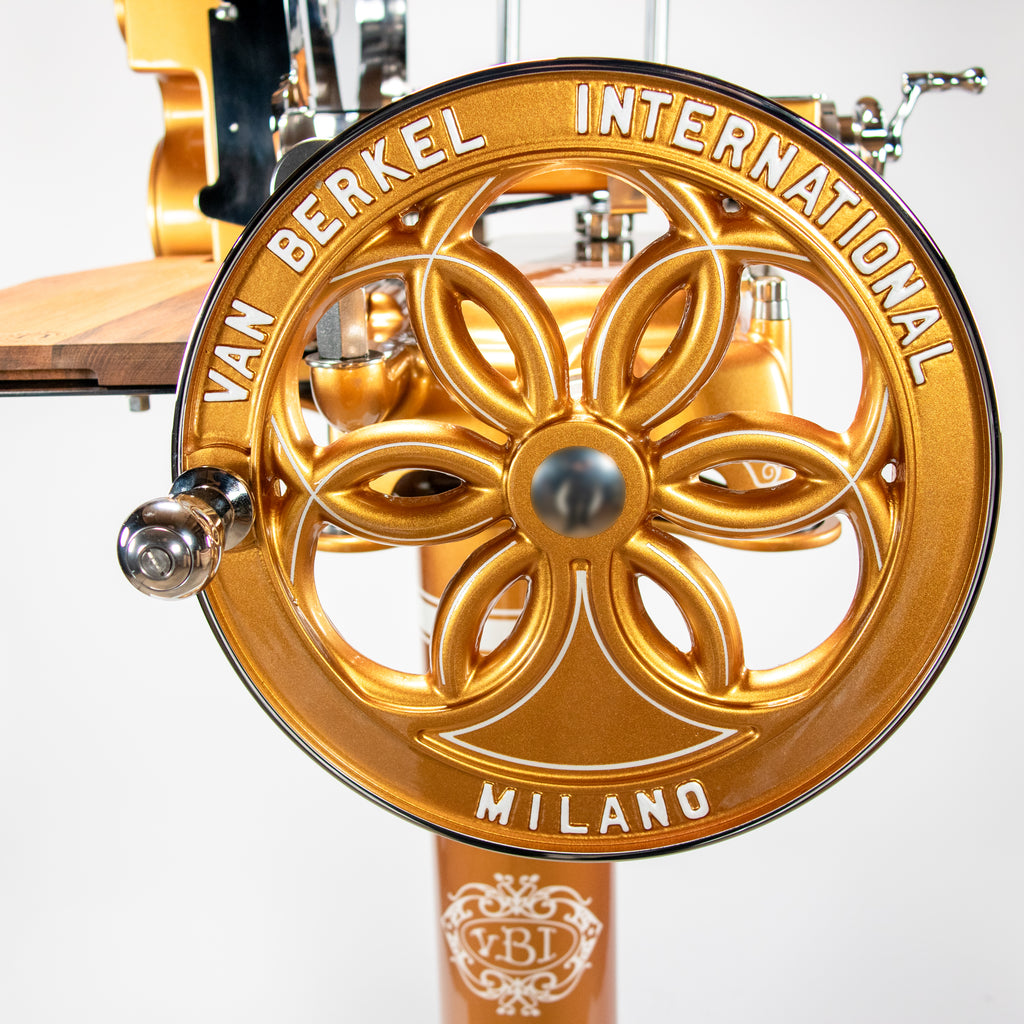 Nahaufnahme des goldenen Schwungrads der Berkel Volano B114 Schwungradmaschine Gold | mit Fassholz-Einlegebrett, mit der Prägung "VAN BERKEL INTERNATIONAL MILANO" um ein dekoratives Blumenmotiv.
