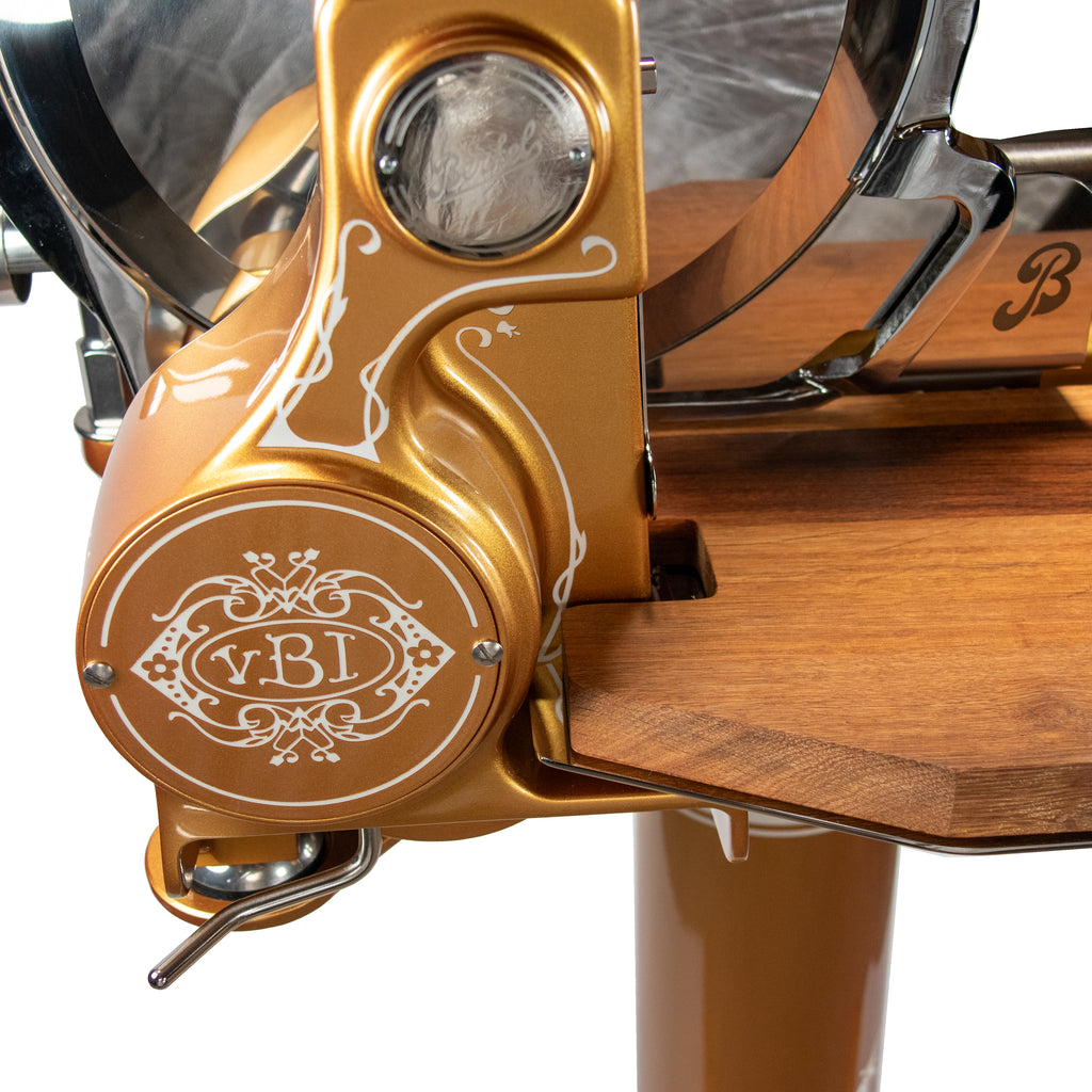 Nahaufnahme der Berkel Volano B114 Schwungradmaschine Gold mit verschnörkelten weißen Details, Holzakzenten und eingravierten Initialen "v.BI" auf einem runden Teil; mit Fassholz-Einlegebrett.
