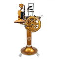 Eine alte Berkel Volano B114 Schwungradmaschine in Gold, mit Fassholz-Einlegebrett und verschnörkelten Details, mit "V.BERKEL INTERNATIONALE MILANO" auf dem großen Rad, stehend auf einem dekorativen Sockelsockel.
