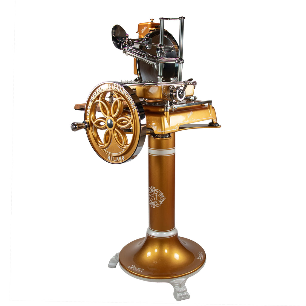 Die Berkel Volano B114 Schwungradmaschine Gold mit Fassholz-Einlegebrett, die sich durch ihre goldene Oberfläche und ihr kunstvolles Design auszeichnet, wird auf einem Sockel vor einem weißen Hintergrund präsentiert.