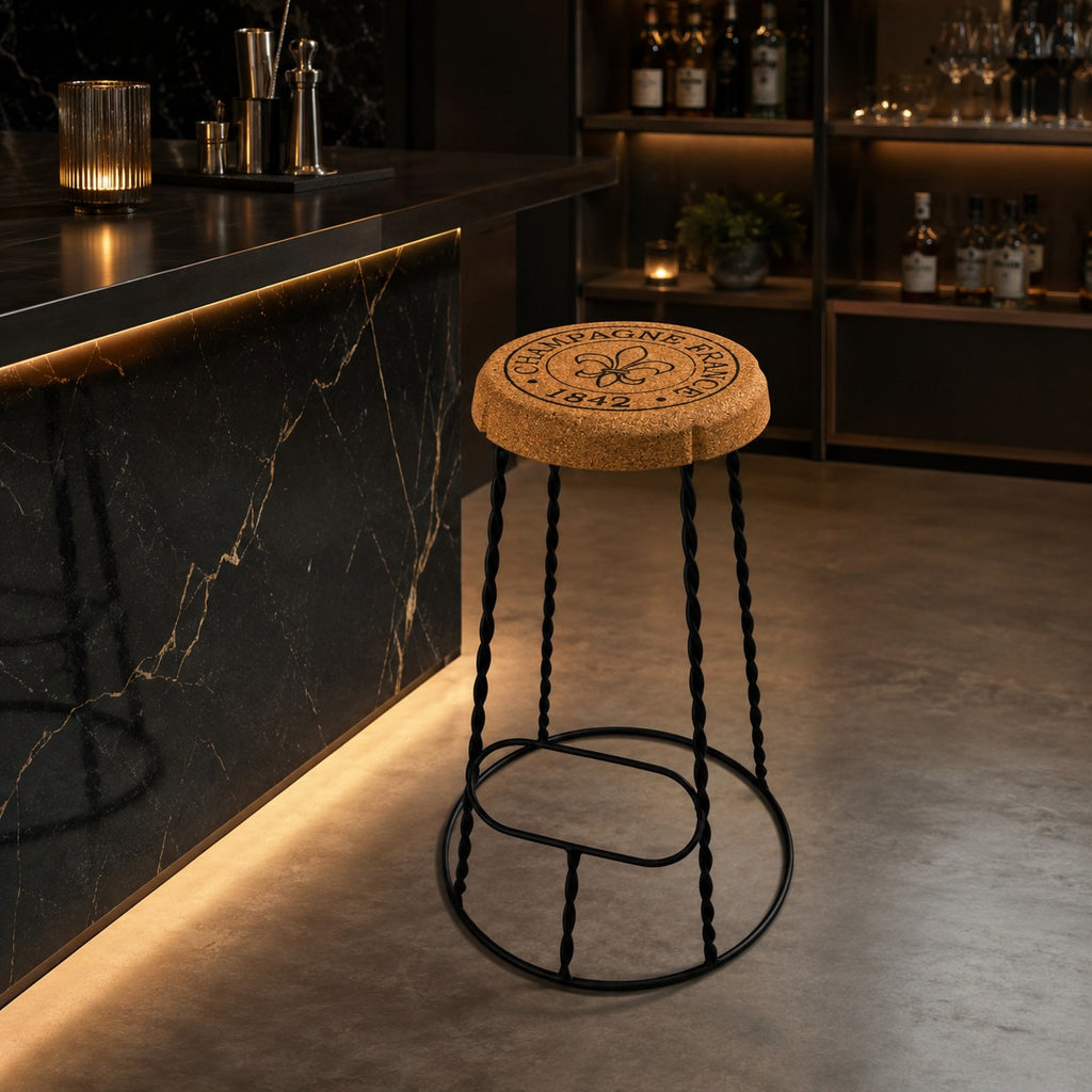 Der hochwertige Barhocker aus Kork und Metall "Agraffe", mit einem korkförmigen Sitz und schwarzen Metallbeinen, steht an einer schwarzen Marmor-Bar in einem modernen, stimmungsvoll beleuchteten Ambiente.