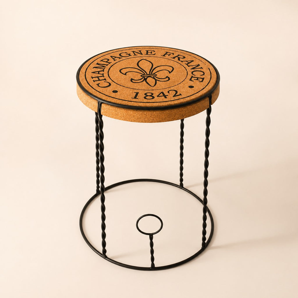 Der hochwertige Beistelltisch aus Kork "Agraffe" hat eine Sitzfläche aus Kork mit der Aufschrift "CHAMPAGNE FRANCE 1842" und einer Fleur-de-Lis, die von schwarzen, gedrehten Metallbeinen getragen wird, die von einem Agraffe-Champagnerkorken auf hellem Grund inspiriert sind.