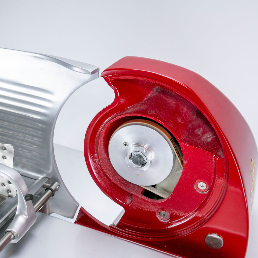 Nahaufnahme einer rot-silbernen Berkel-Schneidemaschine mit freiliegender Klinge. Die glänzende Metallklinge befindet sich auf der rechten Seite, umgeben von der Schutzabdeckung und dem Berkel Messerabnehmer für die Home Line-Serie. Der Hintergrund ist eine schlichte, hellgraue Oberfläche.