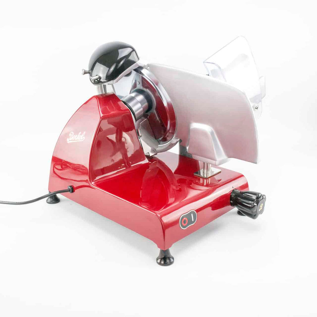Der Berkel Red Line 250 Rot, Allesschneider + handgefertigtes Fassholzbrett aus alten Weinfässern (Eiche), ist vor einem weißen Hintergrund ausgestellt. Dieser rot-silberne elektrische Fleischschneider verfügt über einen schwarzen Griff und Netzschalter und besticht durch ein schlankes, geschwungenes Design mit einem durchsichtigen Schutz über der Klinge. Das Netzkabel ist sichtbar und an der Rückseite eingesteckt.