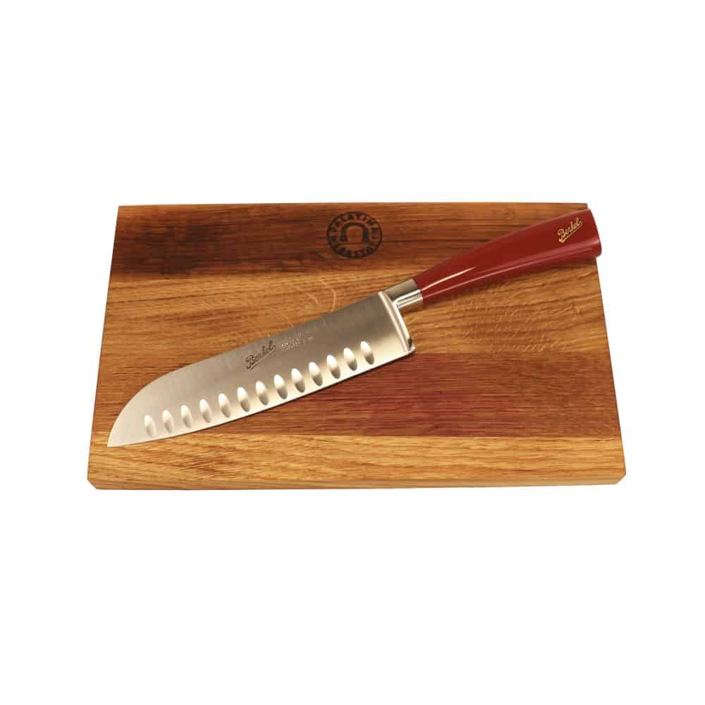 Ein Berkel Messer - Elegance Santoku-Messer 18 cm rot ruht auf einem 100 % handgefertigten Schneidebrett Unikat 30 x 18 cm, das mit einem Logo verziert ist. Das japanische Messer hat eine gerade Klinge mit hohlen Einkerbungen entlang einer Seite, während das Schneidebrett ein wunderschönes helles und dunkles Holzmaserungsmuster aufweist.