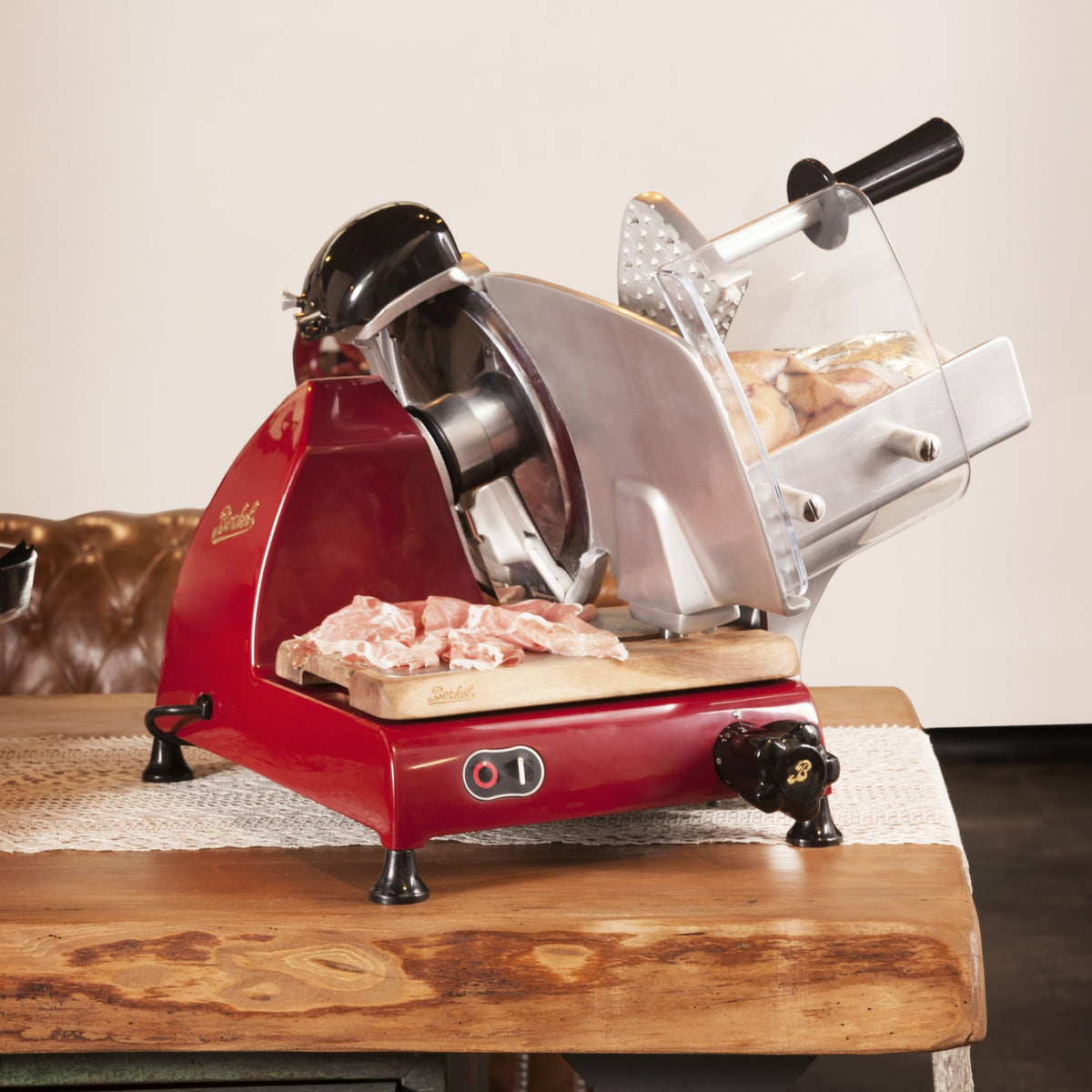 Ein Berkel Red Line 250 Rot Allesschneider schneidet rohes Fleisch auf ein handgefertigtes Eichenbrett, das aus alten Weinfässern hergestellt wurde. Der rote Allesschneider steht auf einem Holztisch, unter dem ein strukturierter Läufer liegt.