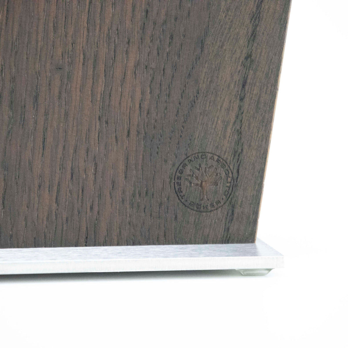 Eine Nahaufnahme des KAI Shun Classic White Damastmesser-Sets, präsentiert auf einem dunklen, glatt strukturierten Magnet-Messerblock von Räuchereiche Böker. Der Block weist ein kreisförmiges geprägtes Logo in der unteren rechten Ecke auf und liegt auf einer weißen Oberfläche, wobei der metallische Sockel darunter teilweise sichtbar ist, was die Eleganz hervorhebt, die Ihr Messerset wunderbar ergänzt.