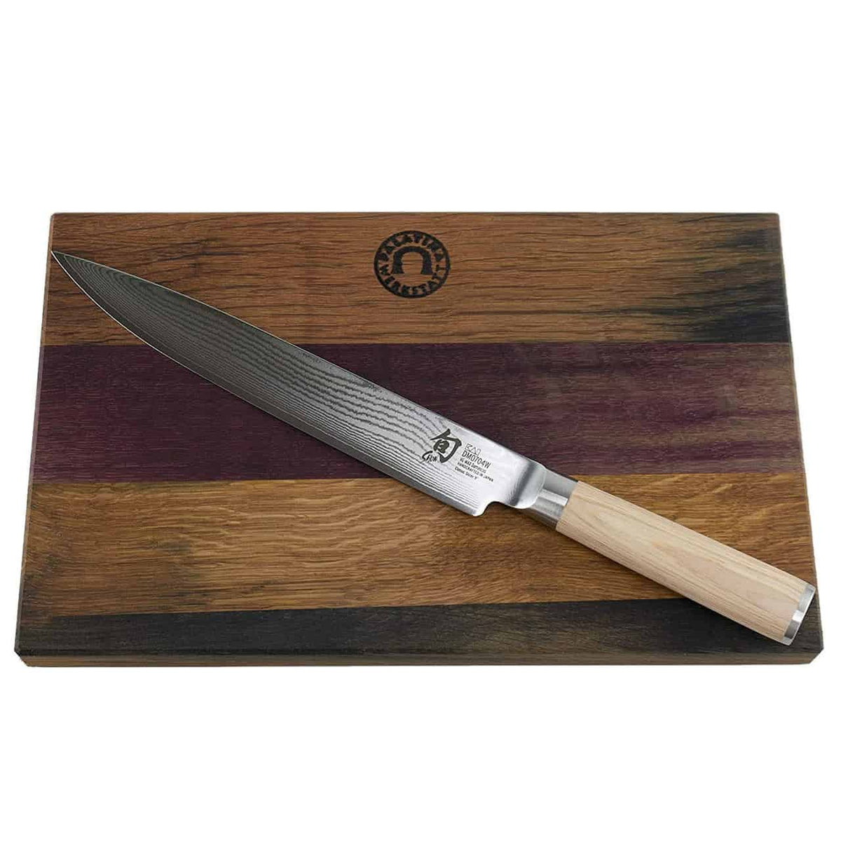Ein Kai Shun Classic White DM-0704W Schinkenmesser mit einer polierten, dunkel gemusterten 23 cm Damastklinge und einem hellen Holzgriff liegt auf einem Fassholz Küchenbrett mit den Maßen 30x18 cm. Das Schneidebrett ist in dunklen und hellen Naturholztönen gehalten, mit leichten violetten Schattierungen akzentuiert und durch ein rundes Logo gekennzeichnet.