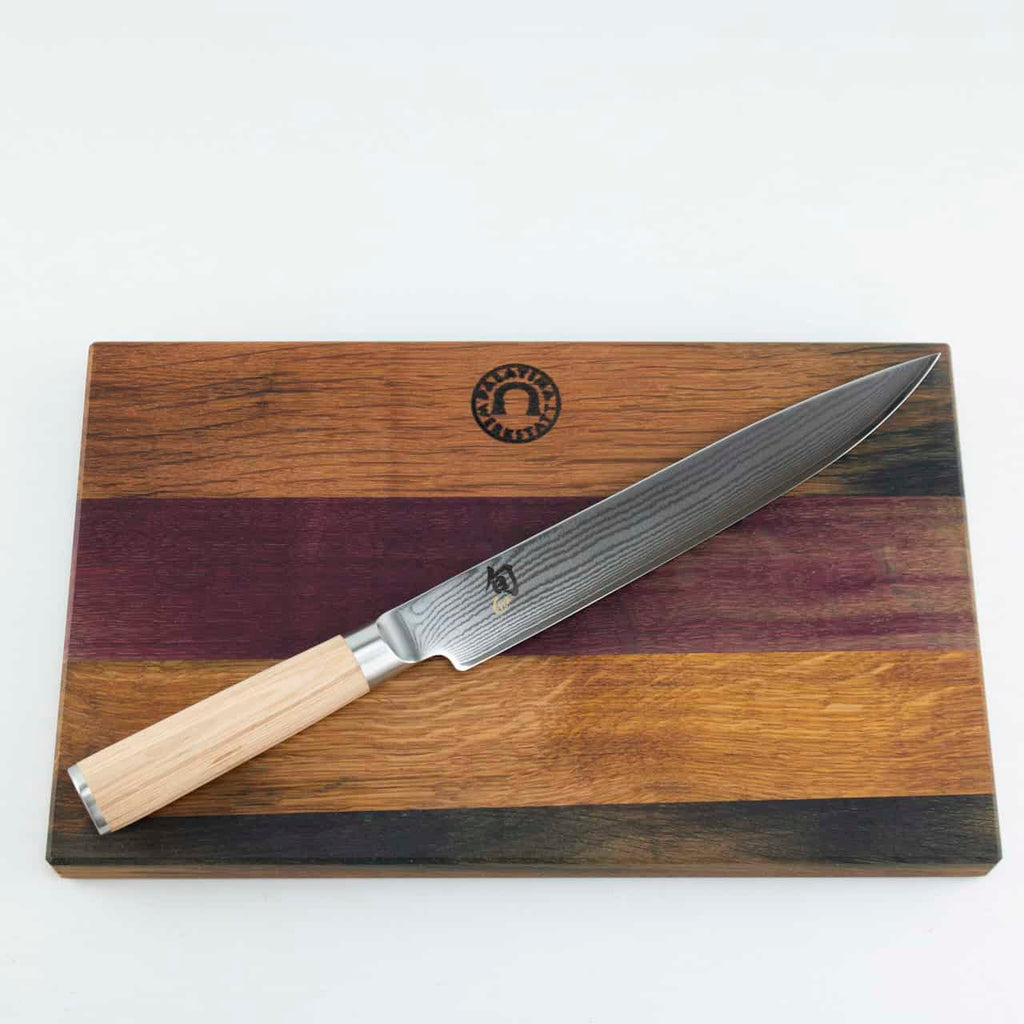 Ein Kai Shun Classic White DM-0704W Schinkenmesser mit einer polierten 23 cm Damastklinge und einem hellen Holzgriff liegt auf einem Fassholz Küchenbrett mit den Maßen 30x18 cm. Das mehrfarbige Holzschneidebrett weist verschiedene Brauntöne auf und hat oben in der Mitte ein Logo, alles vor einem schlichten weißen Hintergrund.
