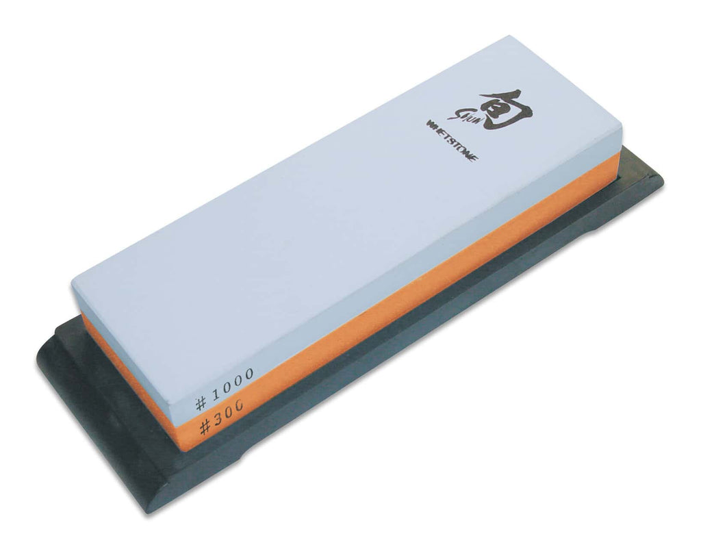 Diese KAI X-MAS SELECTION DREAMBOX Shun Classic White Santoku + Schleifstein enthält einen doppelseitigen Schleifstein mit einer robusten schwarzen Basis. Der obere Stein ist hellblau mit Körnung #1000, ideal für präzises Schärfen, während der untere orangefarbene Stein mit Körnung #300 für gröbere Aufgaben geeignet ist – perfekt, um die Schneide Ihres Shun Classic White Santoku zu pflegen.