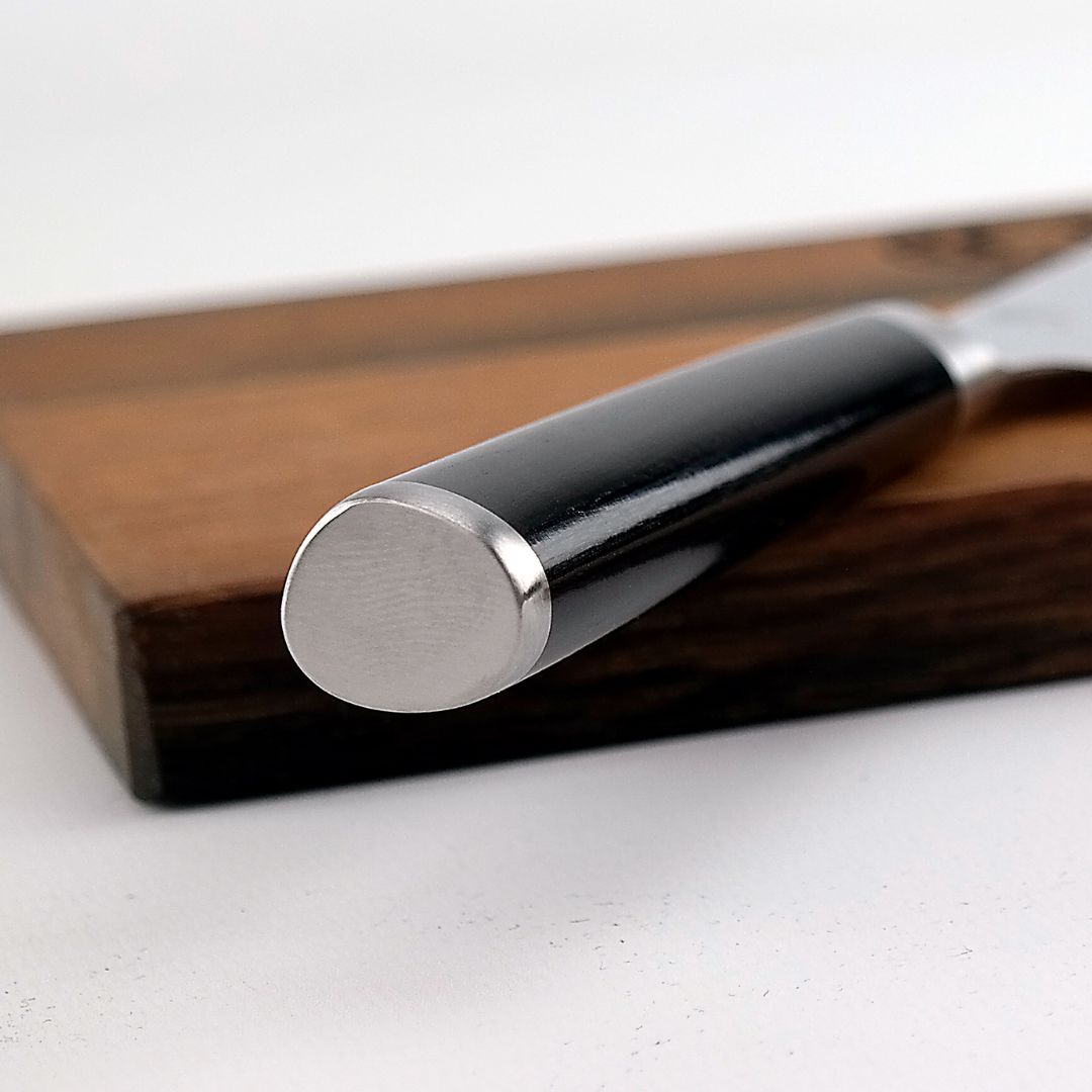 Nahaufnahme des polierten Metallendes des Kai Shun Classic Nakiri Messer Sets - DM-0728 16,5 cm Damast (32 Lagen) mit Griff, das elegant auf dem mitgelieferten 30x20cm Eichenbrett vor einem weißen Hintergrund ruht.
