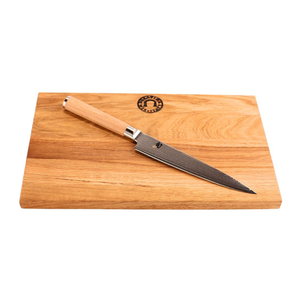 Das Kai Shun Classic White DM-0701W Allzweckmesser (15 cm Klinge) mit Holzgriff liegt diagonal auf dem Weinfass Küchenbrett (30x20 cm) mit Logo, das auf einem klaren, minimalistischen weißen Hintergrund steht.