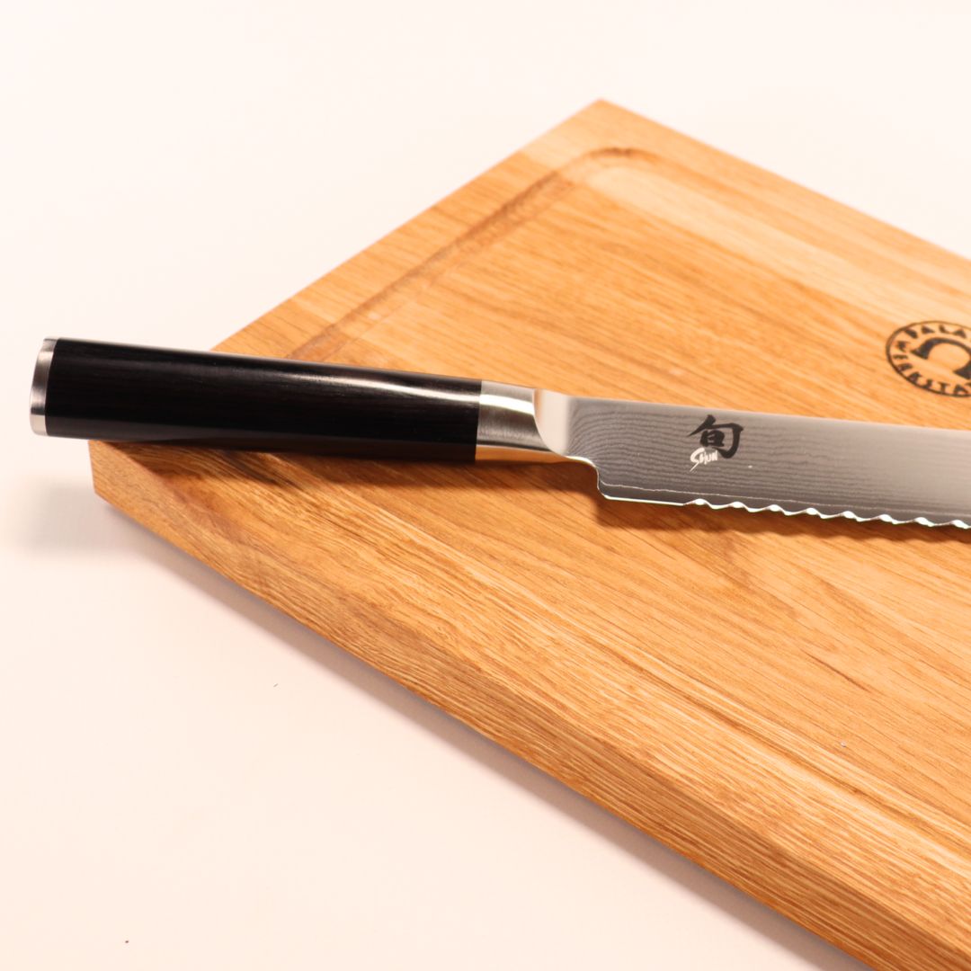 Das Kai Shun DM-0705 Brotmesser (23 cm Klinge) mit dunklem Griff liegt auf dem 30x22 cm großen Eichenholzbrett; das Brotmesser trägt japanische Gravuren - perfekt, wenn Sie ein japanisches Brotmesser kaufen möchten.