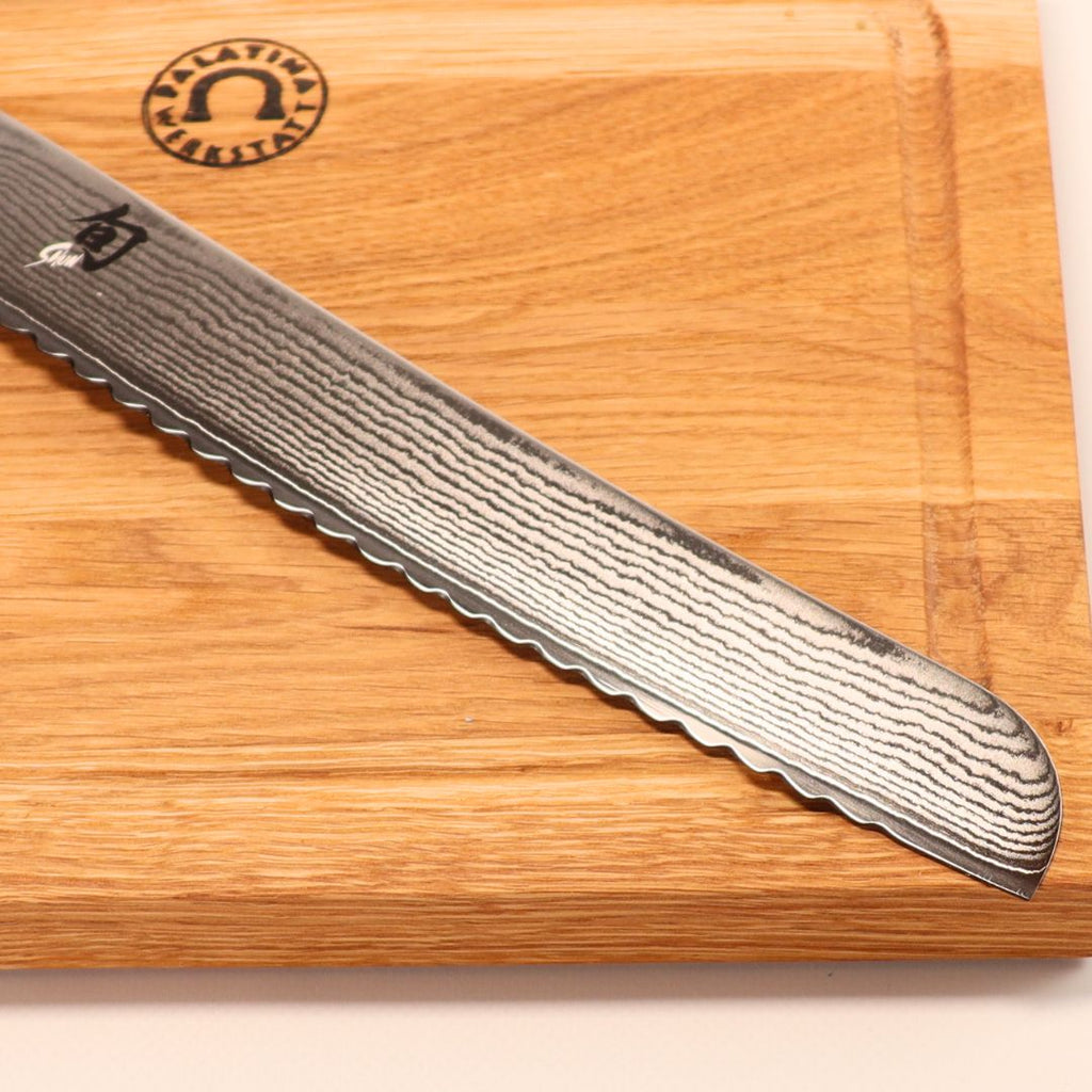 Ein Kai Shun DM-0705 Brotmesser (23 cm Klinge) mit markanter Wellenstruktur liegt diagonal auf dem 30x22 cm Eichenholzbrett.