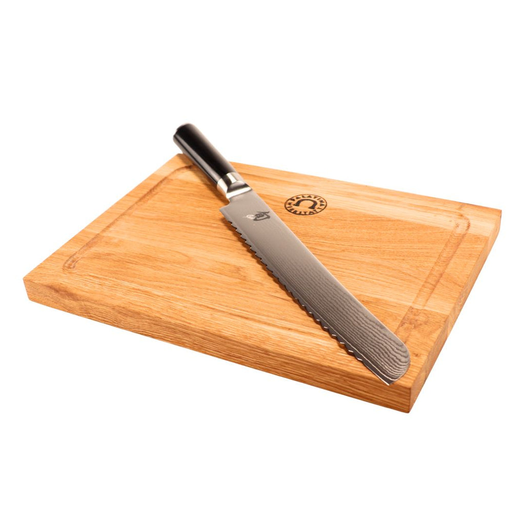 Das Kai Shun DM-0705 Brotmesser (23 cm Klinge) mit schwarzem Griff liegt schräg auf dem 30x22 cm Eichenholzbrett mit Rille und Logo - ideal für alle, die ein japanisches Brotmesser kaufen möchten.
