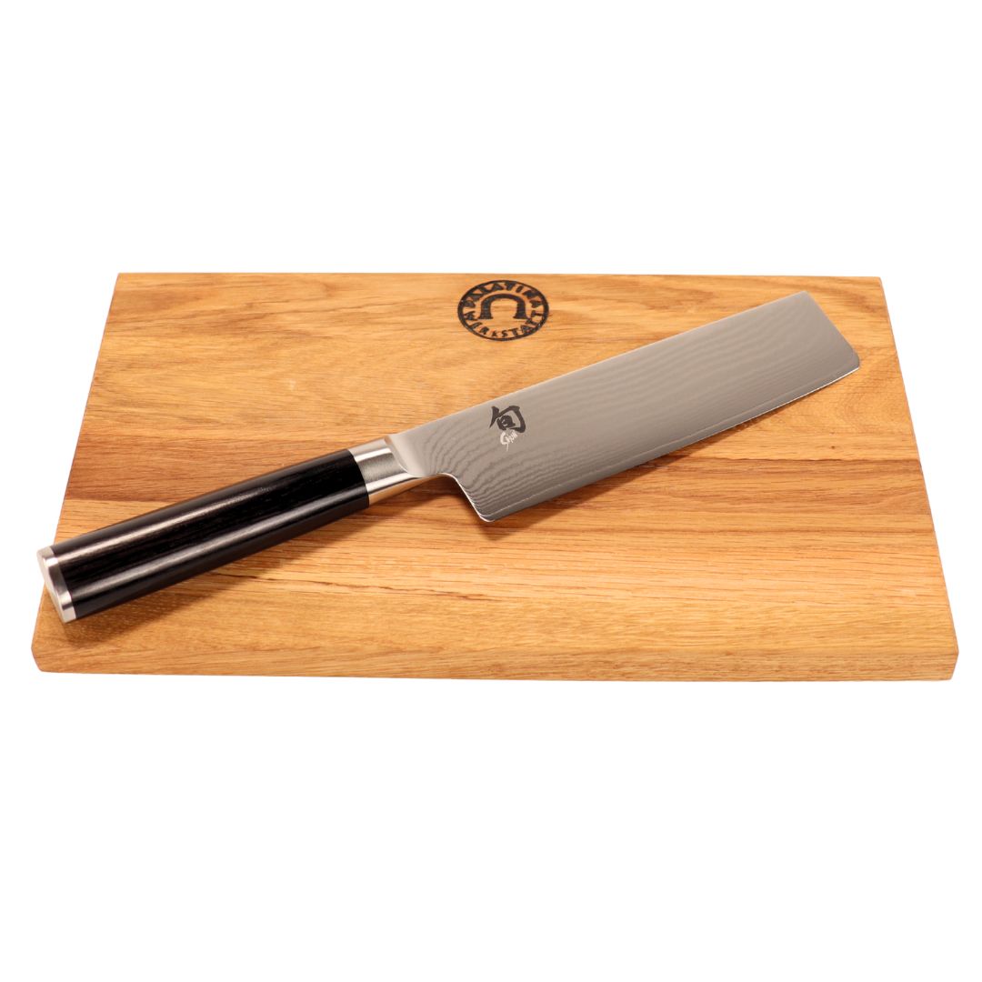 Das Kai Shun Classic Nakiri Messer Set (DM-0728, 16,5 cm, 32-lagiger Damast) besteht aus einem silbernen Messer mit schwarzem Griff, das auf einem 30 x 20 cm großen, rechteckigen Schneidebrett aus Eichenholz mit einem runden Logo am oberen Rand liegt.