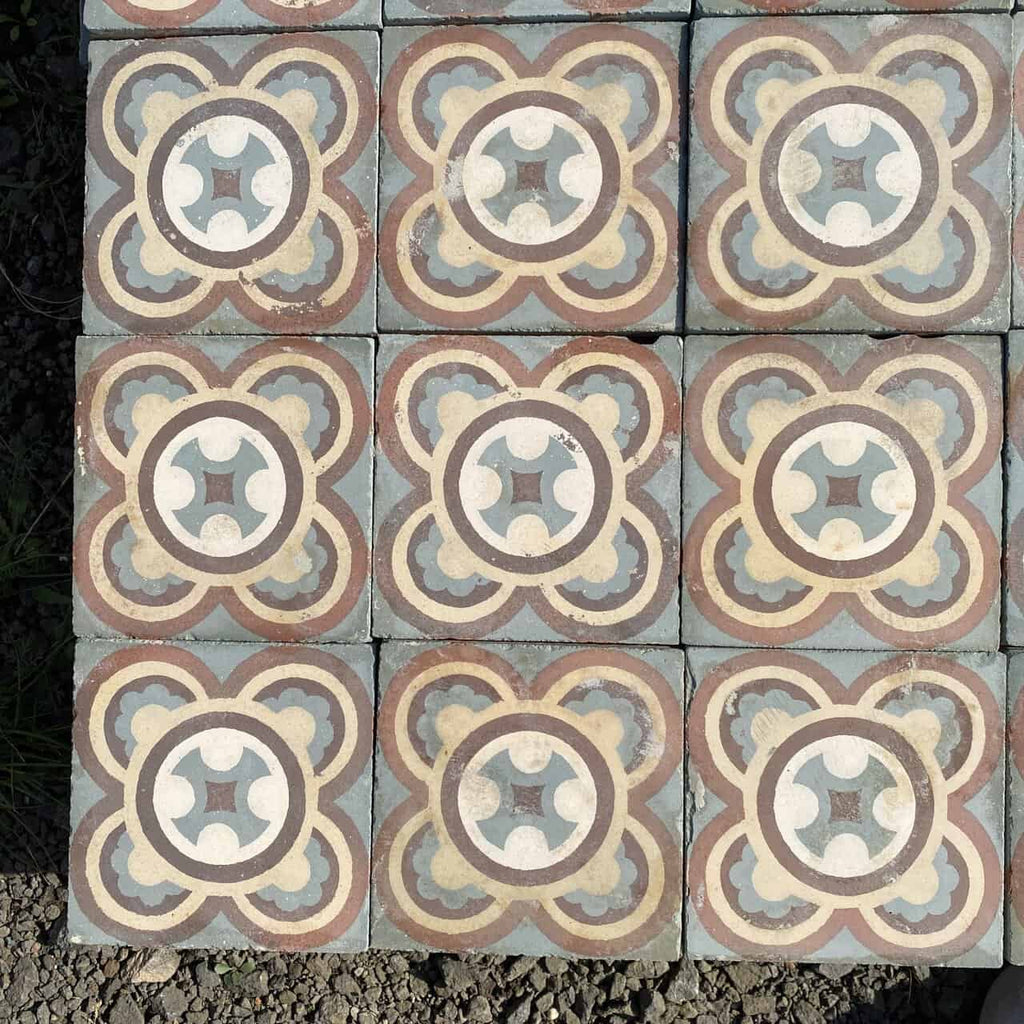 Ein Raster aus historischen Gründerzeitfliesen, wobei jede 16,5 x 16,5 cm große Fliese ein kompliziertes symmetrisches Muster in Blau-, Beige-, Creme- und Brauntönen aufweist. Inspiriert von historischen Fliesen zeigt jedes Stück ein zentrales kleeblattähnliches Motiv, umgeben von ineinandergreifenden kreisförmigen Formen vor einem strukturierten grauen Steinhintergrund. Das gesamte Paket umfasst ungefähr 5,5 Quadratmeter.