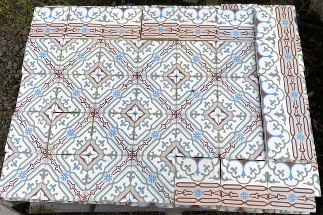 Eine Detailansicht verzierter Bodenfliesen mit einem sich wiederholenden geometrischen Muster, darunter die Historischen Gründerzeit-Fliesen 16,5 x 16,5 cm (Kopie). Das Design umfasst braune, grüne und blaue Elemente auf weißem Hintergrund, die komplizierte Formen und symmetrische Motive bilden, die an die Präzision des Berkel Volano B114 Sondermodells Journey erinnern. Die Fliesen sind in einem rechteckigen Layout angeordnet.