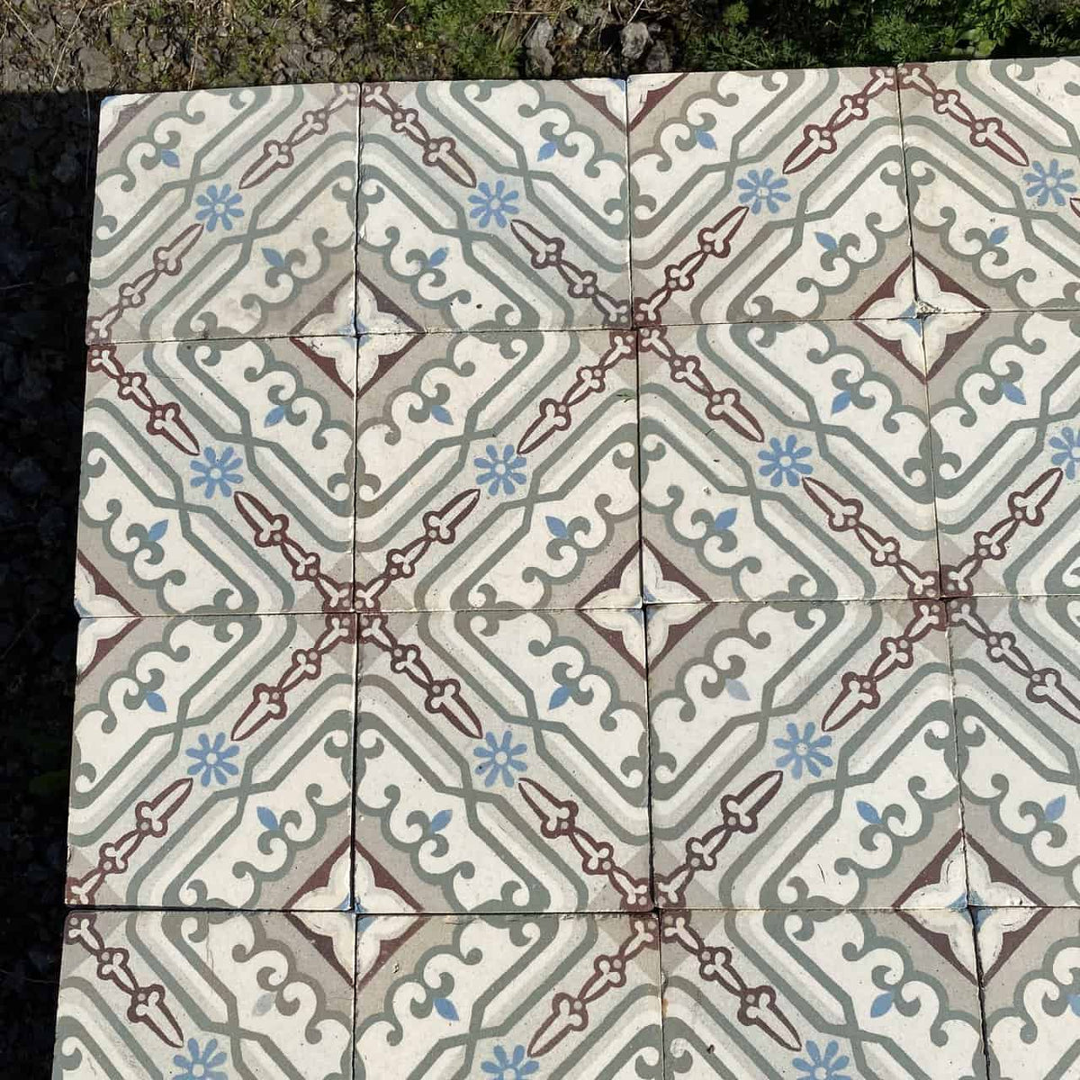 Ein Abschnitt Historischer Gründerzeitfliesen, 14 x 14 cm groß und etwa 10 Quadratmeter groß, zeigt ein geometrisches und florales Design in Erdtönen, darunter Beige-, Braun-, Blau- und Grüntöne. Das Muster weist zentrale Rauten, geschwungene Linien und kleine florale Motive auf, die an historische Fliesen erinnern und einen sich wiederholenden dekorativen Effekt erzeugen.