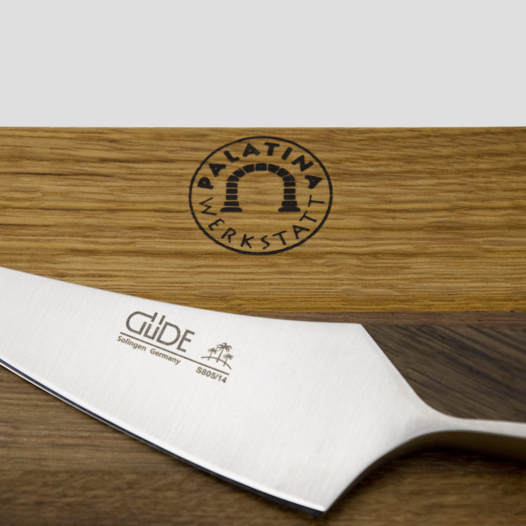Eine Nahaufnahme eines Güde Synchros Zubereitungsmessers, 14 cm Klinge mit Edelstahlklinge und Griff, ruht auf einem handgefertigten Fassholzbrett (34 x 21 cm). Das Schneidebrett trägt das Logo „PALATINA WERKSTATT“, in das wunderschön eine gewölbte Türgrafik eingraviert ist.