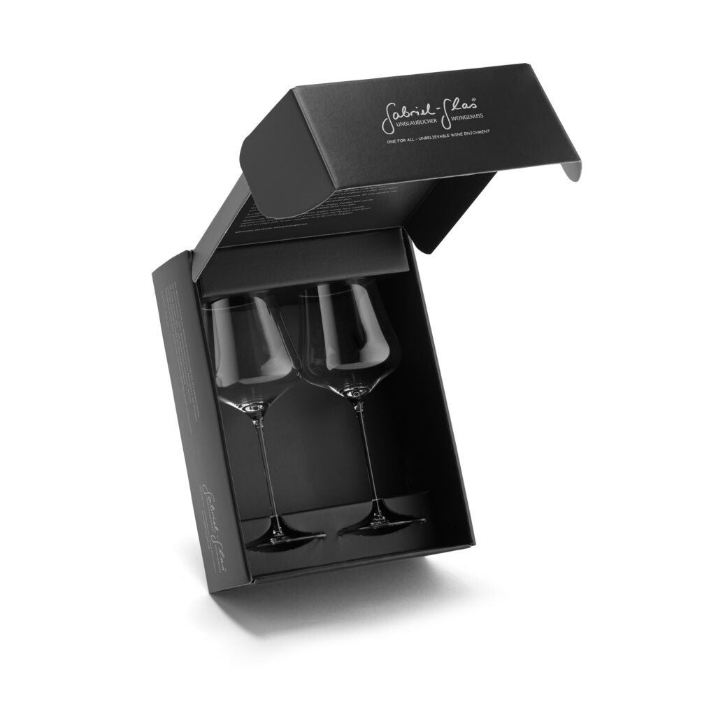 Eine elegante schwarze Box ist teilweise geöffnet und präsentiert zwei elegante Gabriel Gold Edition Weingläser Universalgläser. Auf dem Deckel der Box befindet sich ein weißer kursiver Text. Die minimalistische und raffinierte Verpackung unterstreicht die luxuriöse Präsentation dieser mundgeblasenen, spülmaschinenfesten Gläser, die jeweils 90 Gramm wiegen und mit einem speziellen Pflegetuch geliefert werden.